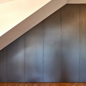 Montuojama mansardinė spinta su varstomomis durimis nuo sienos iki sienos, nuo grindų iki lubų.