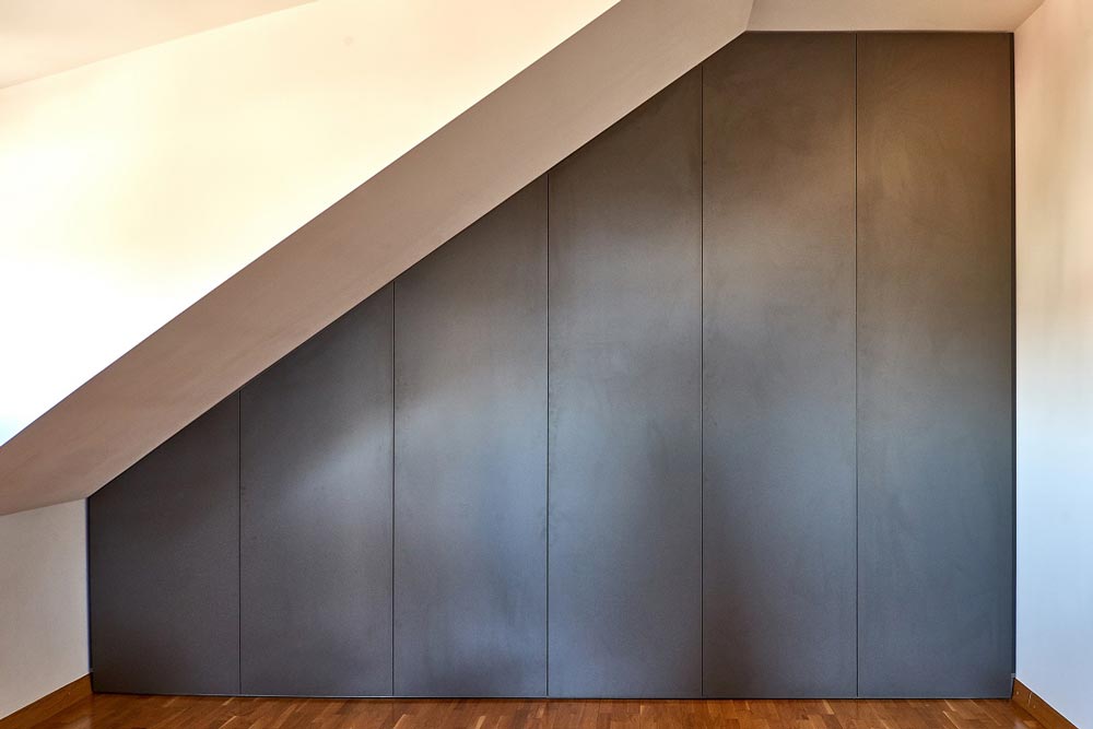 Montuojama mansardinė spinta su varstomomis durimis nuo sienos iki sienos, nuo grindų iki lubų.